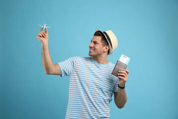 Sticker - Male tourist holding passport with ticket and toy airplane on turquoise background