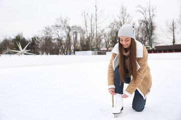 Poster - Woman lacing figure skate on ice rink. Space for text