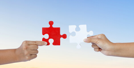 Hands holding piece of red and white jigsaw puzzle on sunset sky background