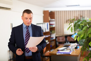 Wall Mural - Concentrated young adult businessman working with documents at workplace in office