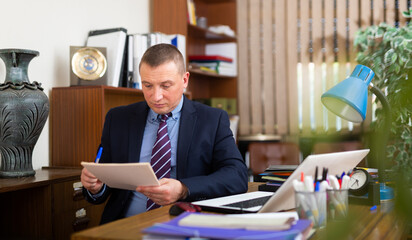 Wall Mural - Concentrated young adult businessman working with documents at workplace in office