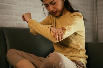 Young Asian discomfort woman holding hand and pressing points of elbow while suffering from elbow joint pain sitting on sofa at home