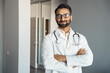 © Stock 4 You - Portrait of male doctor wearing white lab coat, stethoscope standing and looking at camera in clinic hall. Arabian indian therapist, general practitioner headshot. Medicine, heal insurance, healthcare