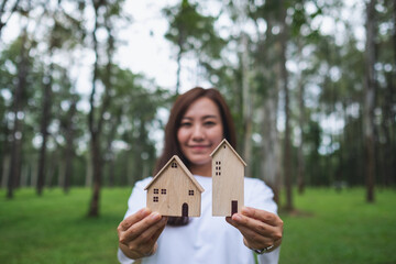 Wall Mural - A beautiful asian woman holding and showing wooden house models in the park