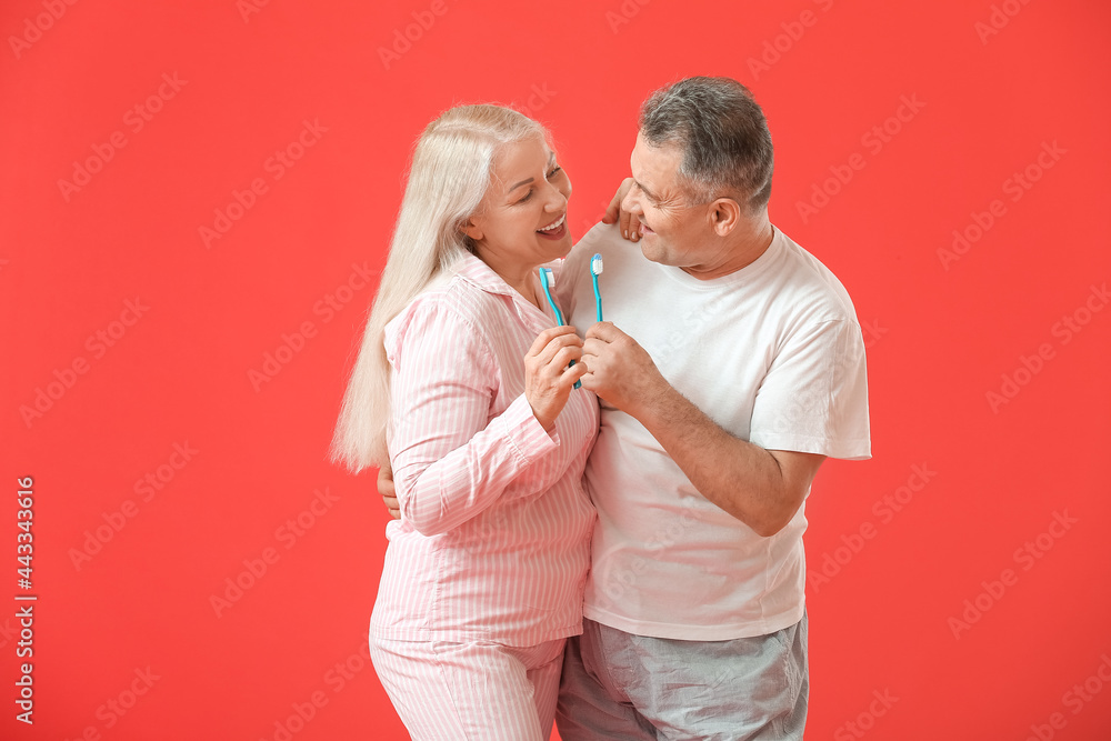 Mature couple brushing teeth on color background