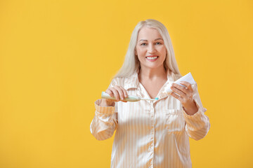 Canvas Print - Mature woman brushing teeth on color background