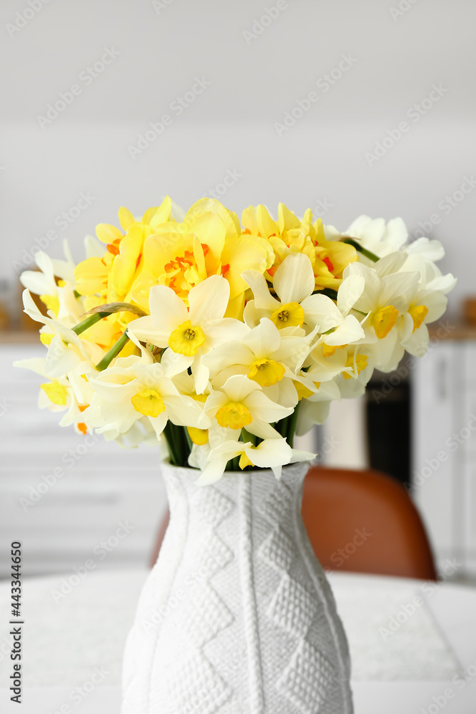 Vase with narcissus flowers on table in kitchen