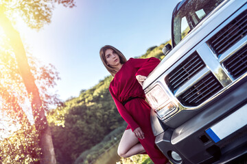 Fashion girl in stylish red dress standing near her modern car and relax ar nature in summer day