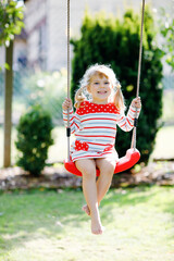 Wall Mural - Happy beautiful little toddler girl having fun on swing in domestic garden. Cute healthy child swinging under blooming trees on sunny spring day. Baby laughing and crying