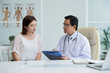 © DragonImages - General practitioner listening to complaints of young woman and taking notes in document on clipboard