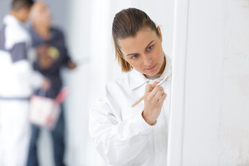 young female apprentice focused on painting wall edge