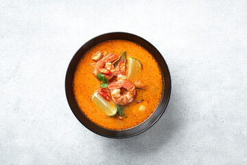 Tom Yum kung Spicy Thai soup with shrimp in a black bowl on a bconcrete background, top view, copy space