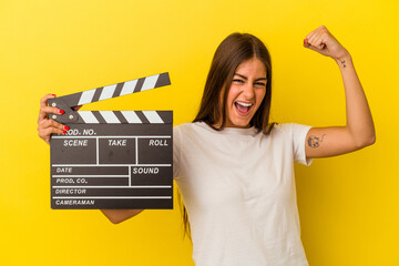 Wall Mural - Young caucasian woman holding clapperboard isolated on white background raising fist after a victory, winner concept.