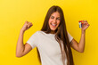 © Asier - Young caucasian woman holding a home keys isolated on yellow background raising fist after a victory, winner concept.