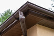 Brown plastic gutter system against sky, roof overhang