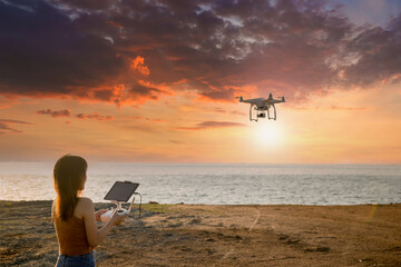 Young woman using drone at sunset for photos and video making - Happy woman having fun with new technology trends in sky and sea.