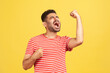 Extremely excited overjoyed man with beard in striped t-shirt shouting making yes gesture, amazed with his victory, triumph. Indoor studio shot isolated on yellow background