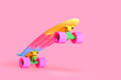 Pastel neon rainbow colored Penny board skateboard standing on two wheels isolated on solid soft pink background. Plastic mini cruiser Youth minimalistic Sport inspired summer fun concept. Copy space.