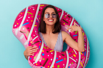 Young caucasian woman with inflatable donut isolated on blue background person pointing by hand to a shirt copy space, proud and confident