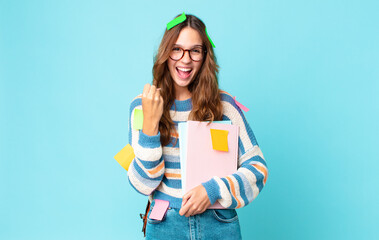 Wall Mural - young pretty woman feeling shocked,laughing and celebrating success with a bag and holding books