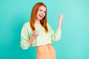 Wall Mural - Photo of lucky funky young woman wear green shirt rising fists smiling isolated teal color background