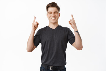 Image of handsome modern man, pointing up and smiling happy, showing company logo, points at brand name and looks pleased, recommends item, white background