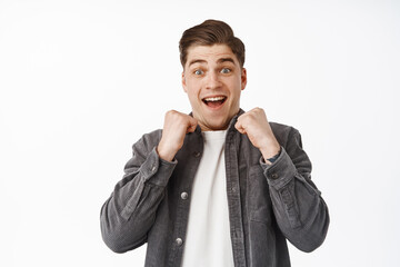 Wall Mural - Close up of surprised and excited guy winning something, looking in awe with hands near chest, cheering, triumphing from win, achieve goal, receive great positive news