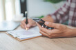 © EduLife Photos - Close-up businessman holding a pen, smartphone and pointing at financial graph checking business report on wooden desk with computer laptop besided at home. Stock photo