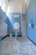A wide angle shot of a toilet with the seat up in a bathroom with blue tiles and white furniture
