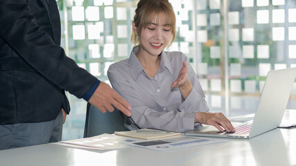 A young financial market analyst works in the office with his laptop while sitting at a wooden desk. Asian businessman analyzing graph document in hand and can calculate the pattern of the company