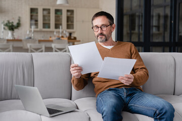 Confident mature man freelancer businessman working from home, doing paperwork online, paying bills, writing reports, checking contracts and documents using laptop remotely