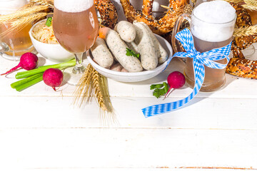 Wall Mural - Oktoberfest food background, Traditional bavarian holiday food menu, sausages with pretzels, sauerkraut, beer glass and mugs on white wooden sun lighted background copy space