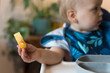 One year old baby holds out a soft strip of cooked eggs; allergenic food exposure Baby Led Weaning