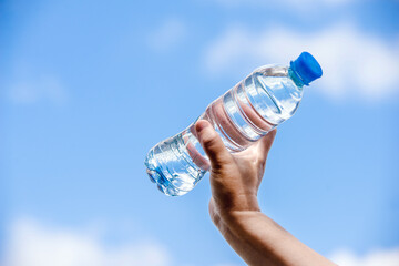 A girl holds a bottle of drinking water in her hand against a blue sky background
