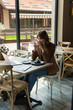 © LIGHTFIELD STUDIOS - young woman in eyeglasses looking at laptop near chocolate cake and drinking coffee in cafe.