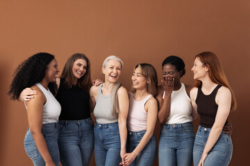 Wall Mural - Stylish women of different ages having fun while wearing jeans and undershirts over brown background