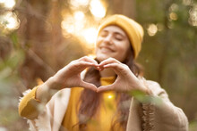 Young Woman Forming A Heart With Her Hands While Smiling, She Is In A Forest In Autumn.