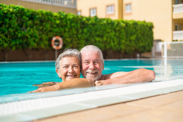 Canvas Print - Couple of two happy seniors having fun and enjoying together in the swimming pool smiling and playing. Happy people enjoying summer outdoor in the water
