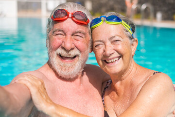 Couple of two happy seniors having fun and enjoying together in the swimming pool taking a selfie picture smiling and looking at the camera. Happy people enjoying summer outdoor in the water.