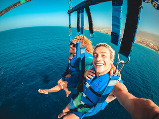 Wall Mural - couple of two happy people enjoying summer and vacations doing extreme activity on the sea with a boat - beautiful people taking a selfie while doing parascending together.