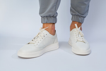 Men's feet in white everyday sneakers made of natural leather on lacing.