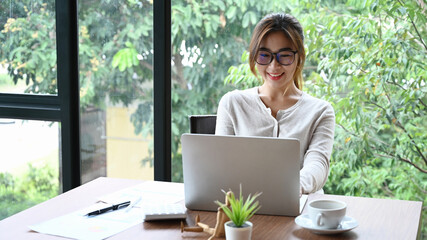 Wall Mural - Smiling young female designer working with computer laptop in modern office room.