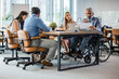 © Dragana Gordic - Happy businessman in wheelchair reading documents during a meeting with his colleagues in the office. Shot of a team of businesspeople having a meeting in a modern office