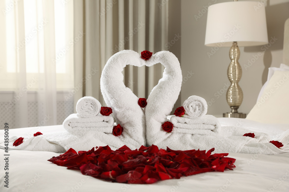 Beautiful swans made of towels and red rose petals on bed in room - obrazy, fototapety, plakaty 