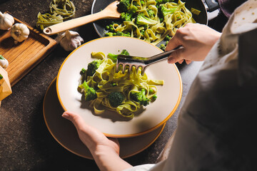 Woman putting tasty pasta with vegetables onto plate at table