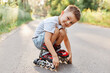 © sementsova321 - Boy in roller skating sitting on the road, looking at camera with smile, wearing white t-shirt and short, child squats while having rest rollerblading.