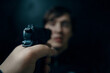 Criminal with gun. First person view of pistol aimed at young man on dark background. Murderer or armed thief. Firearm in man's hand. POV of aiming at human target.