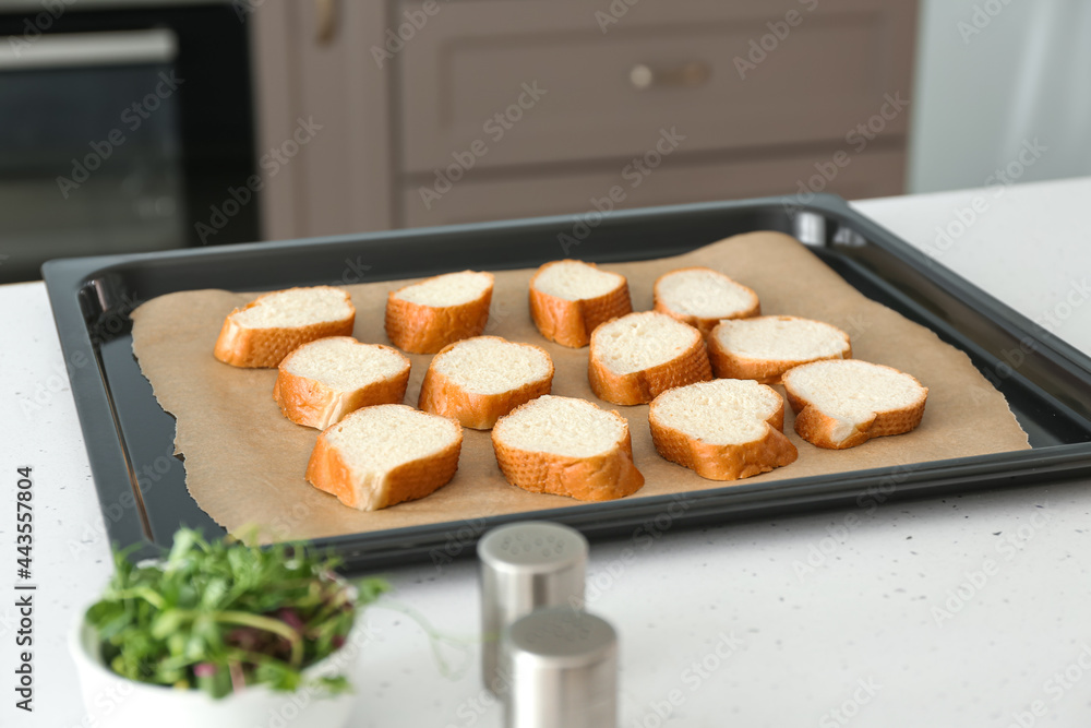 Baking sheet with slices of fresh bread on kitchen table
