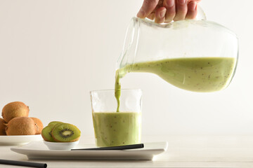 Wall Mural - Person serving kiwi drink from jug on table isolated white