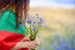 Woman covered with flag of Lithuania holding bouquet of blue cornflowers in a rye field. Lithuanian Flag Day. Independence restoration Day. King mindaugas day.